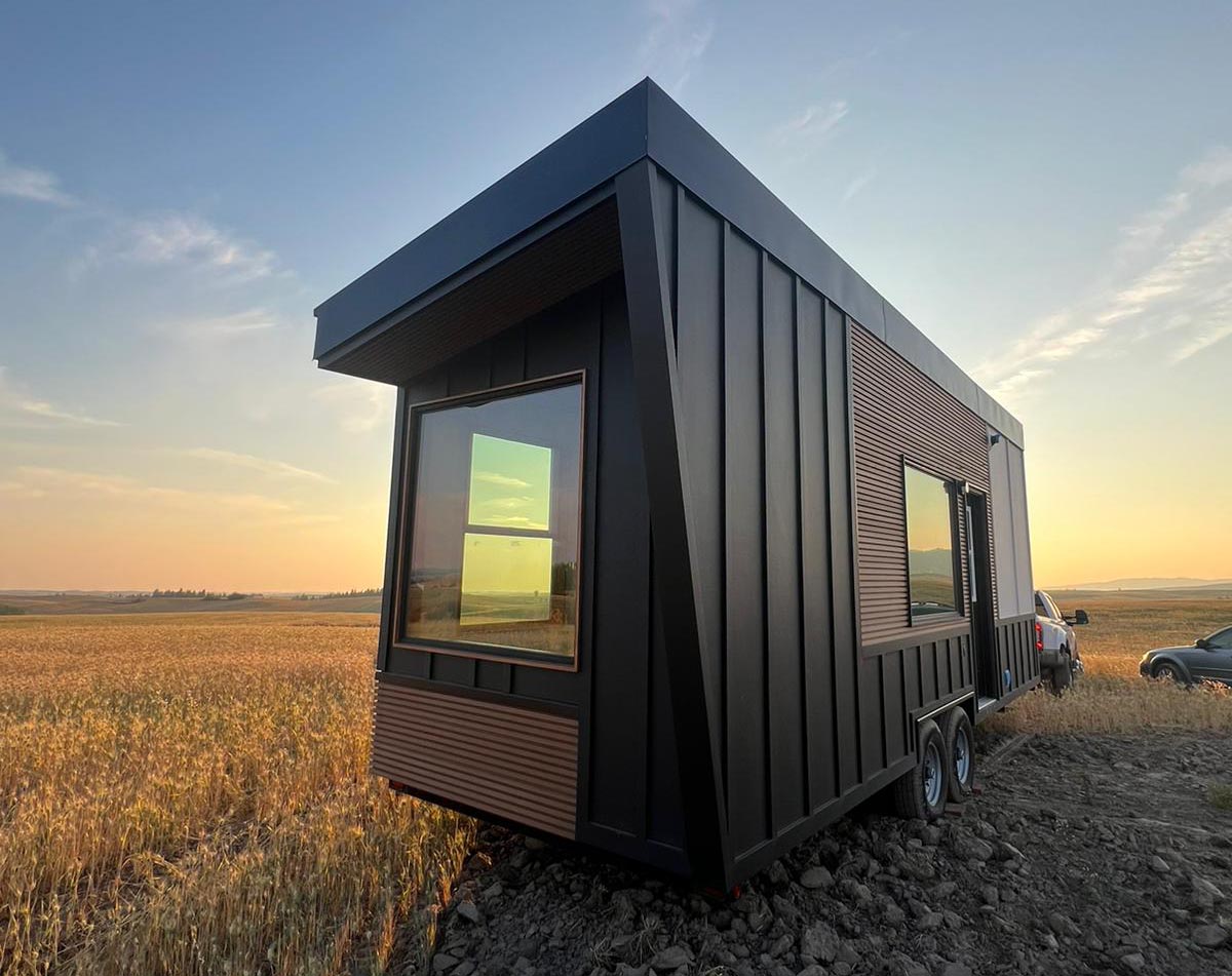 Photo of a tiny home on wheels parked in a picturesque farm overlooking the sunset