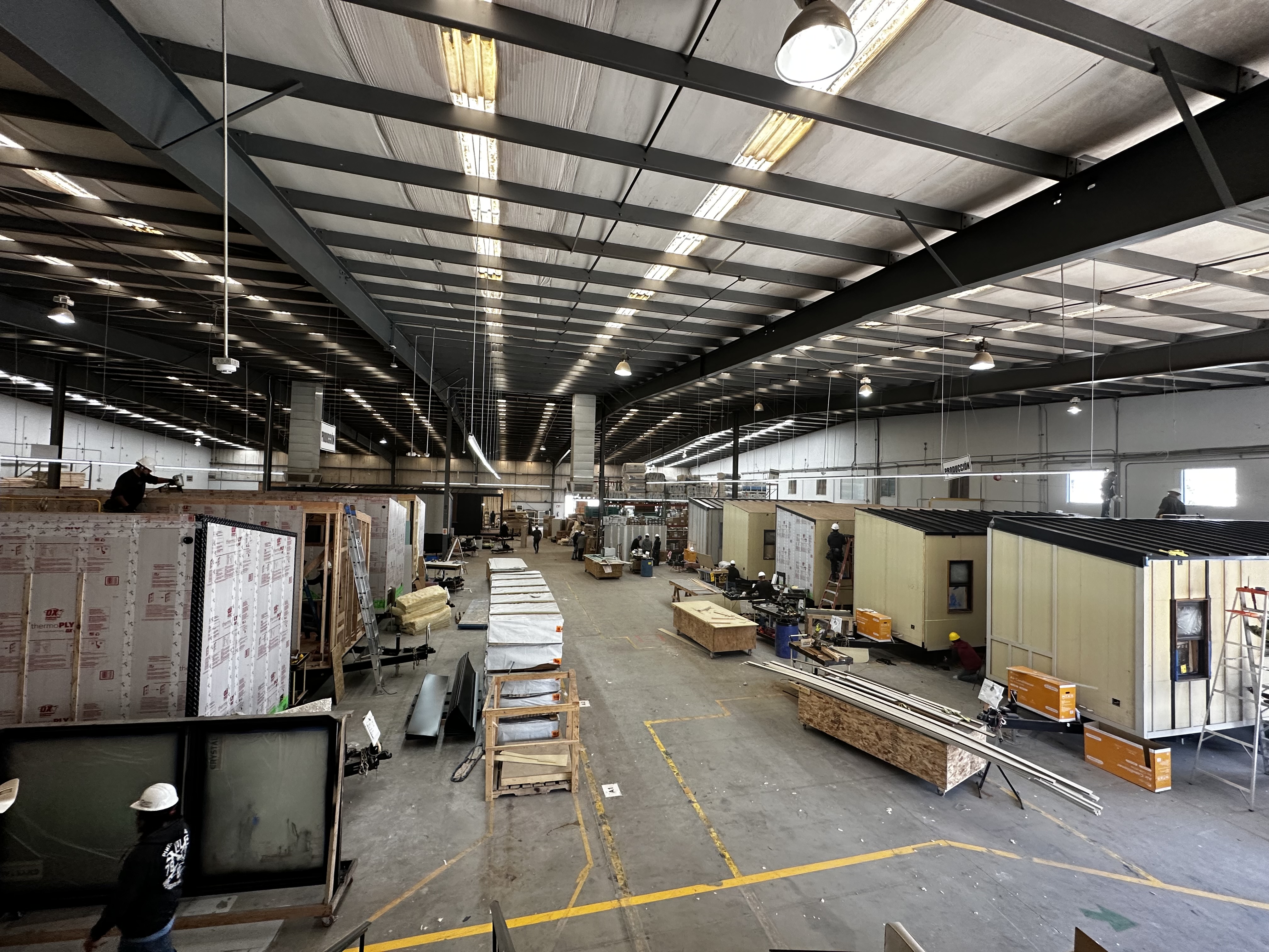 Rows and rows of partially constructed tiny homes aligned in a factory setting, each home is in a different stage of construction, with uniform framing and materials organized nearby, reflecting the streamlined workflow and precision of this tiny home company.