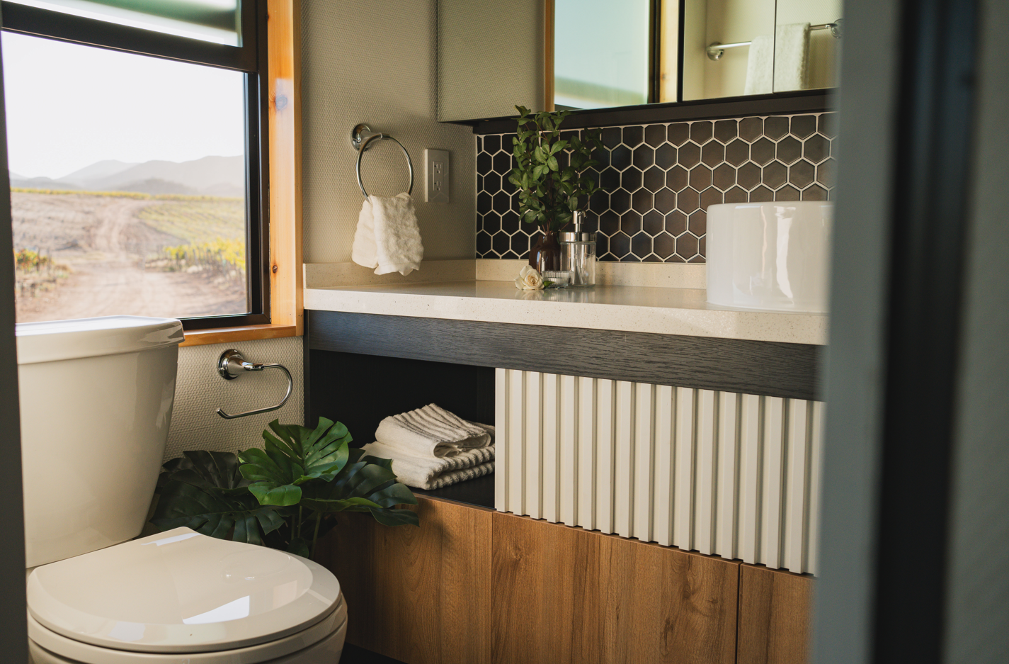 Modern tiny home bathroom with full-size vanity mirror, glass shower, and built-in storage by Clever Tiny Homes.