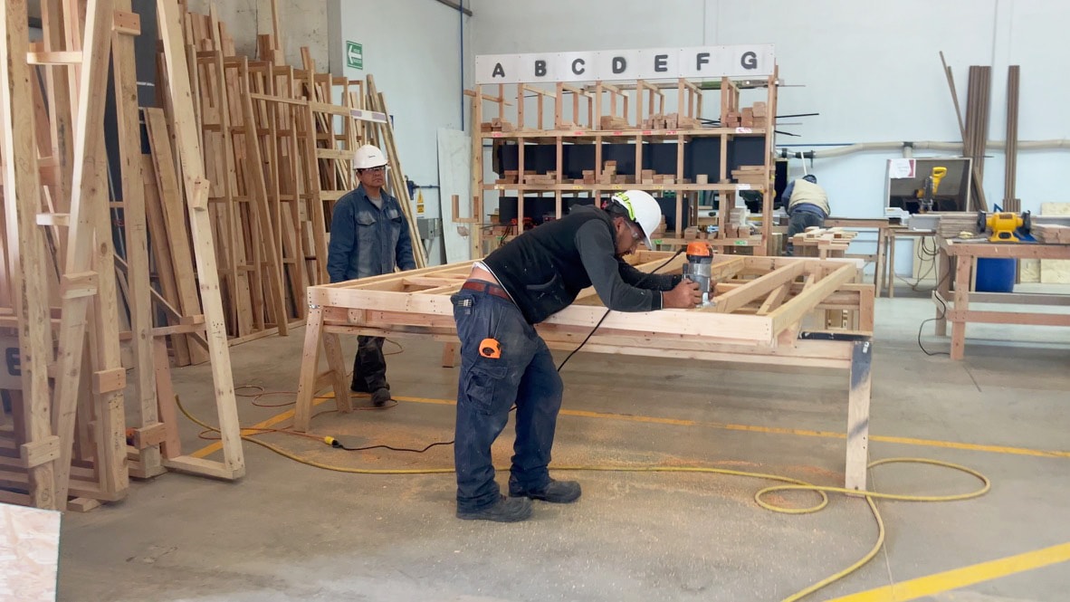 Scenes from a modern tiny home factory, with men working on a frame.