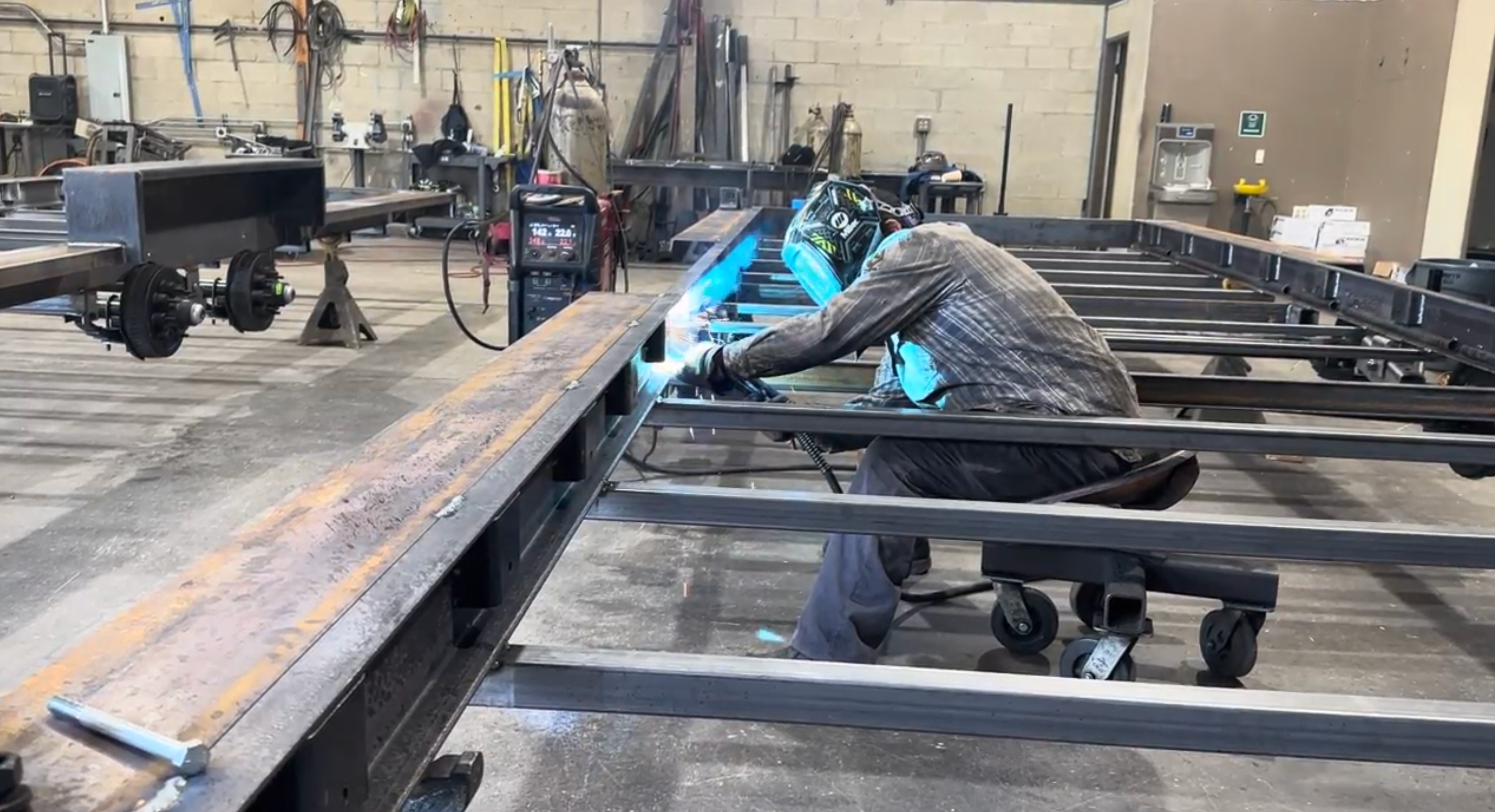 A man welding a trailer chassis used for tiny homes on wheels.