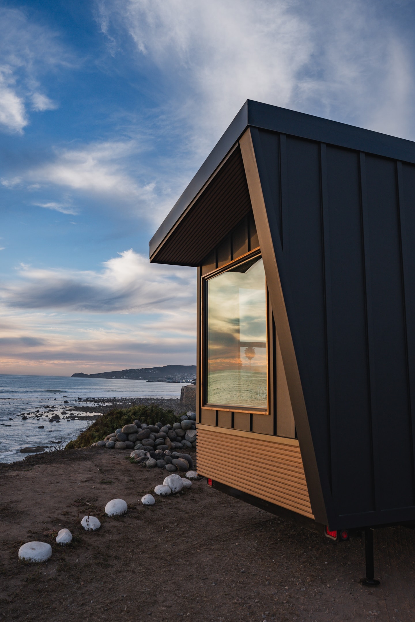 Close up of a tiny home's large windows with the sea and sky reflected on it.