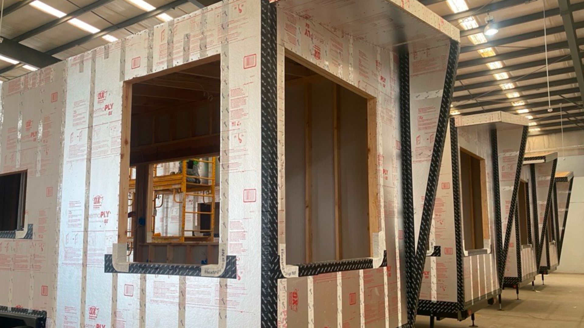 Rows of partially constructed tiny homes aligned in a factory setting.