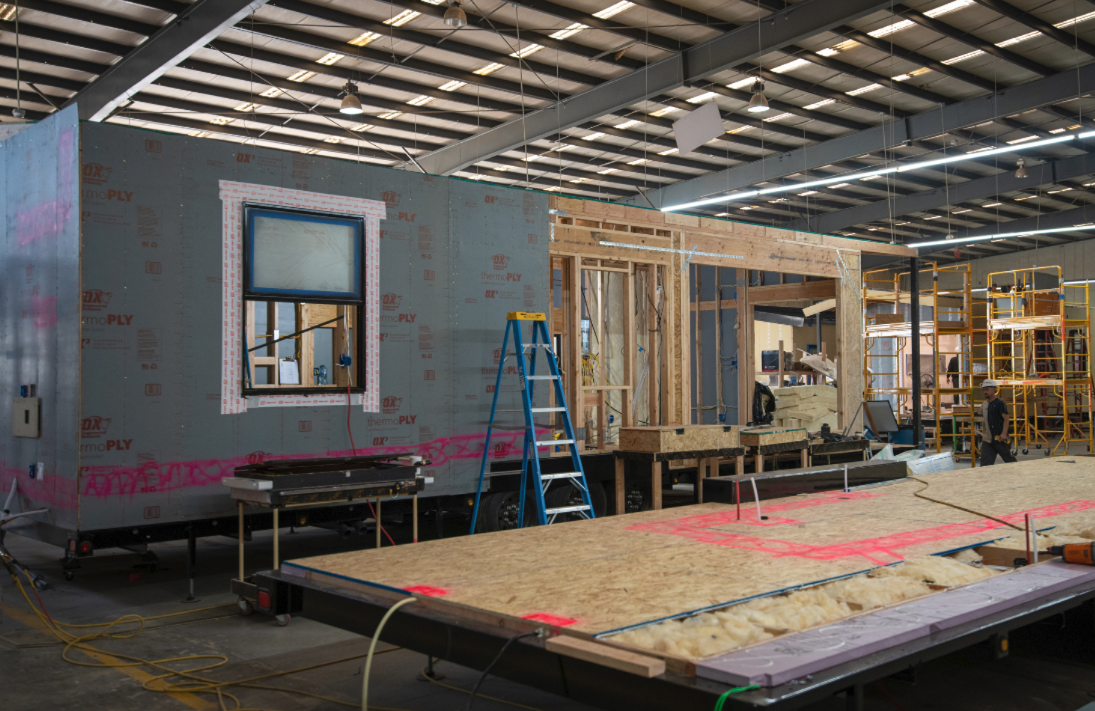 Factory workers assembling modular home sections under controlled indoor environment.