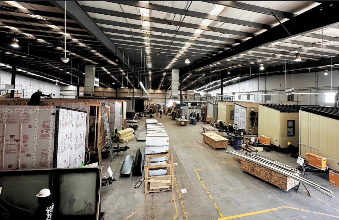Construction team inspecting modular home unit at factory assembly line.