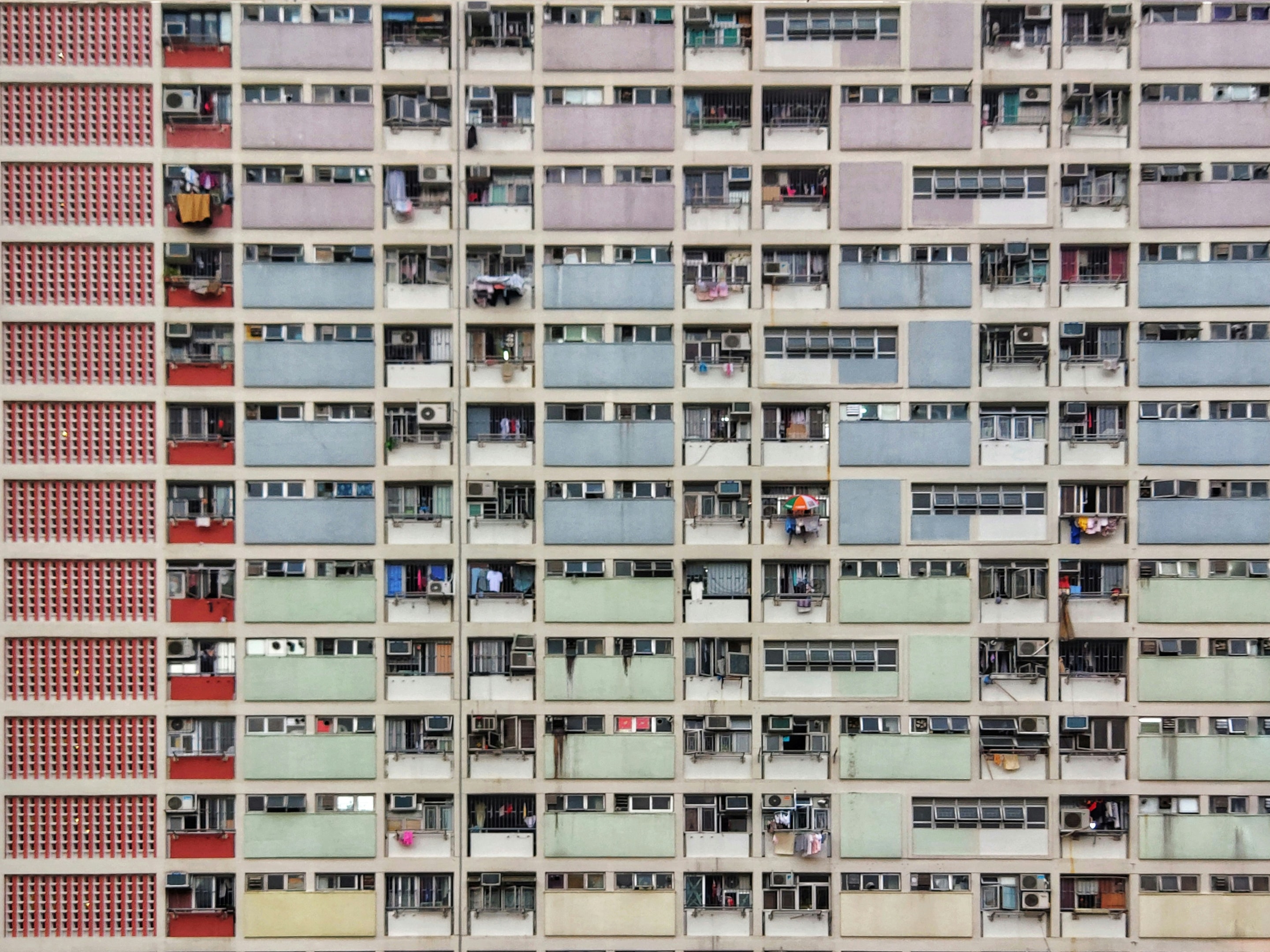 A vibrant shot of Choi Hung Estate in Hong Kong highlights Asia's approach to compact living, with multi-story apartments in pastel hues, urban greenery, and a bustling basketball court. 