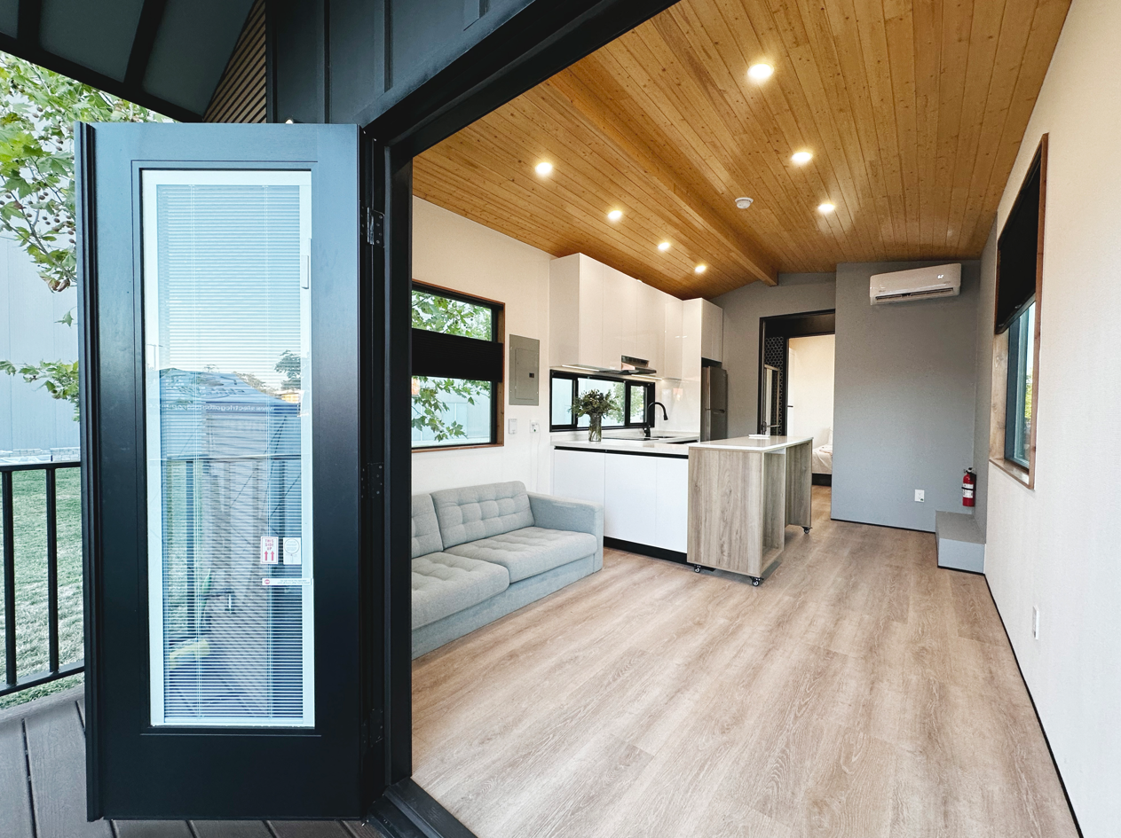 Interior of a modern tiny home with huge windows, cathedral ceilings, full kitchen and main floor bedroom